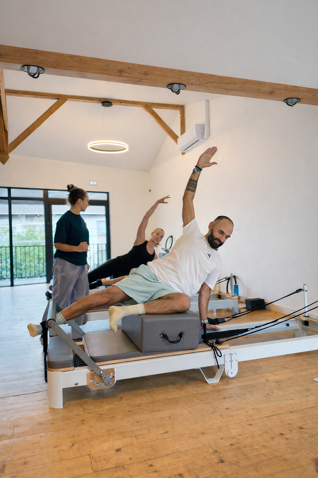 Cours de Pilates Reformer: deux élèves font une plancha latérale sur l'équipement, supervisés par leur instructeur dans un studio lumineux.